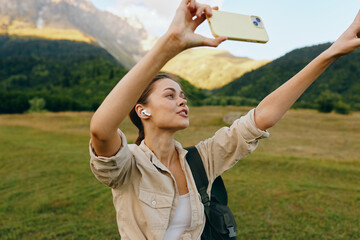Fototapeta premium Bright outdoor moment with a woman lifestyle outdoors selfie in a mountain nature travel smiling casual portrait, sunlit backdrop and lush scenery