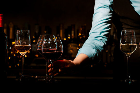 Close up of woman hand taking glass of red wine from bar counter. Selection of different wines for professional degustation.