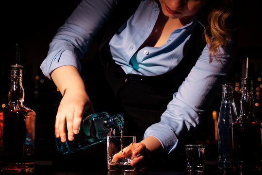Woman bartender preparing cocktail with gin and tonic in bar. Professional mixology and drink preparation.