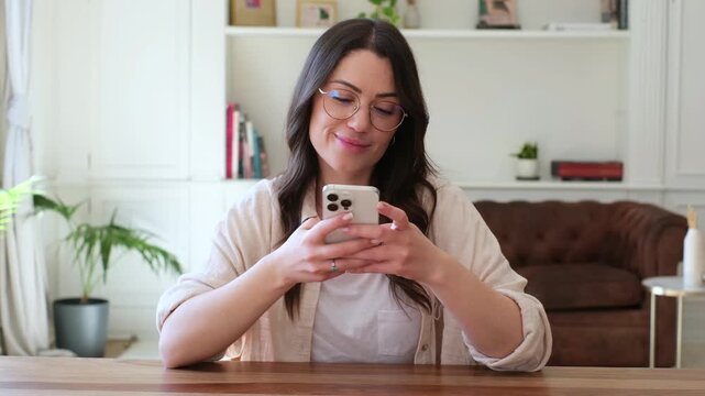 A calm young woman in glasses engages with her smartphone, browsing content with a gentle smile before looking up in contemplation, perhaps pondering new ideas or enjoying a moment of thought at hom