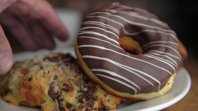 Manipulacion de alimentos, imagen de acercamiento a una mano agarrando pan dulce de un plato en una mesa con una taza de te o cafe en el fondo, con pared de ladrillo fuera de foco.