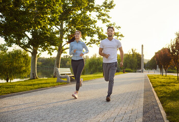 Obraz premium Happy smiling sporty couple wearing sportswear jogging in the park having sport workout. Young man and woman running outdoors. Workout in nature, exercising and healthy lifestyle concept.