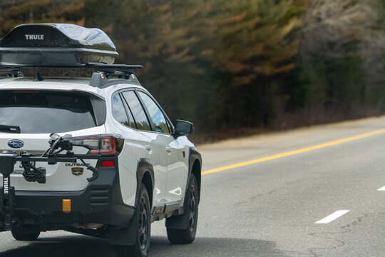 Quebec, Canada, 24 April 2026 : White Subaru Outback SUV with Thule roof box and bike rack drives on a road.