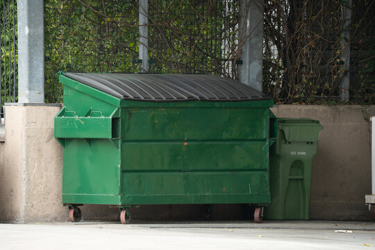 Large green dumpster and smaller trash bin next to a concrete wall