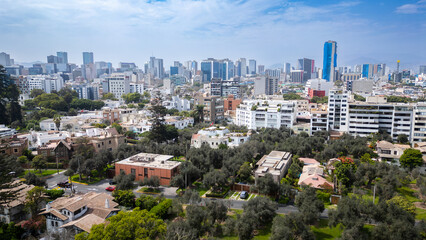Obraz premium Vibrant panoramic view of San Isidro's financial district skyline viewed from the lush canopy of the historic El Olivar park in Lima, Peru.