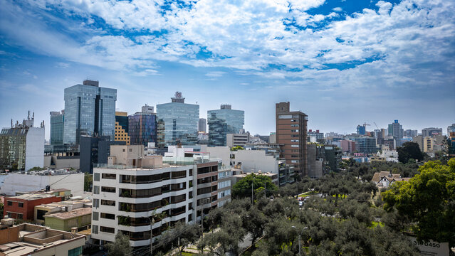 Wide aerial view of the urbanized and modern district of San Isidro, showcasing the mix of residential homes and high-rise buildings on a bright, sunny day in Lima, Peru.