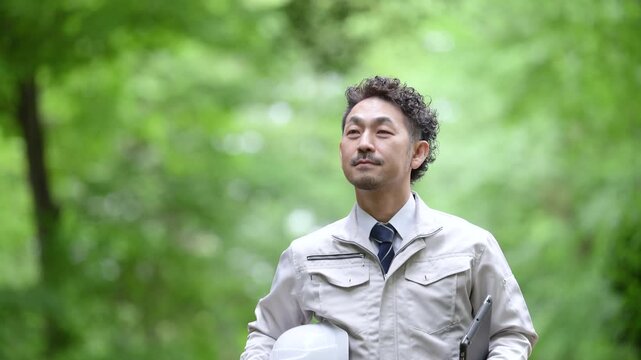 新緑の中の都市計画のインフラ、林業や施工管理などの現場作業員がヘルメットとタブレットを持って歩く動画スローモーション