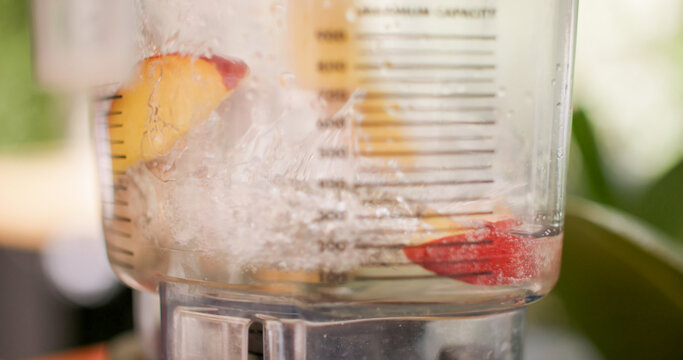 Pouring water blender. Fruit drink preparing. Fresh peaches pieces in automatic machine covering with alcohol syrup liquid in professional bar.