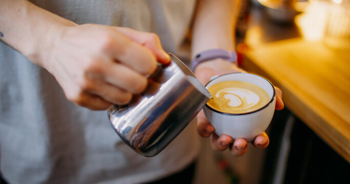 Latte art. Coffee shop. Male barista hand pouring milk from metal pitcher to cup making heart shape pattern on drink in cafeteria.