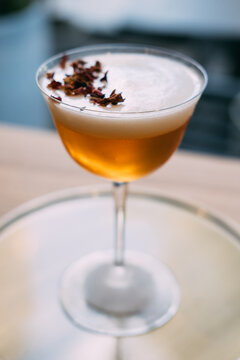 Rose cocktail. Aperitif glass. Amber sour whiskey served on tray. Bar drink with whipped white top dried flower buds aromatic garnish.