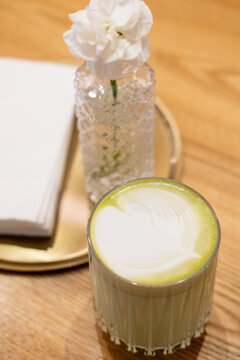 Green tea. Cold drink. Traditional asian herbal matcha served with milk foam served on restaurant wooden table near flower in vase.