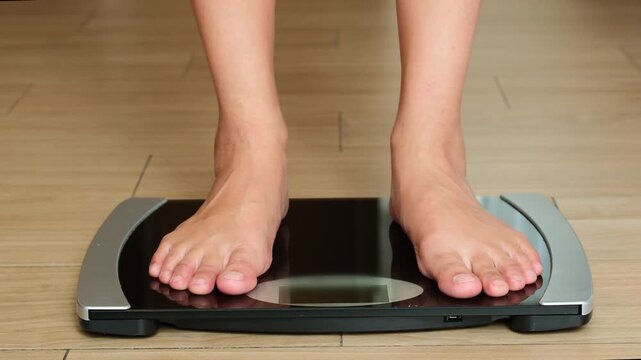 Bare feet of man standing on a black, analog bathroom scale on a light wooden floor. The person is checking their weight, concept focusing on health, fitness, and diet monitoring	