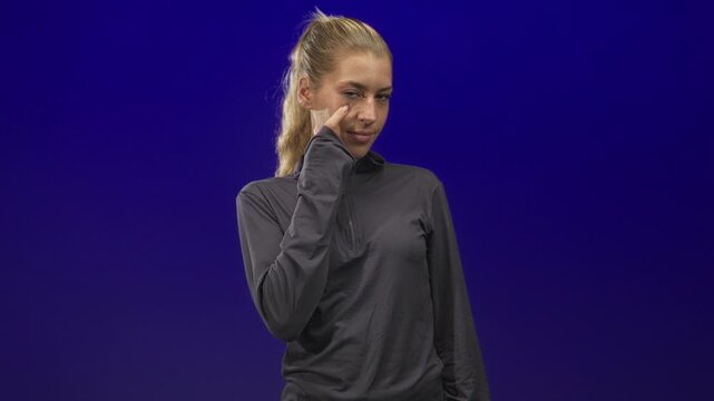 Woman touching cheek with index finger in studio wearing dark pullover, slight smile and soft gaze; thoughtful.
