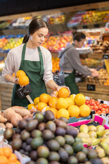 Fototapeta premium Saleswoman lays out grapefruits on the counter in a supermarket. Saleswoman checks the quality of citrus fruits against the background of the interior of a grocery store