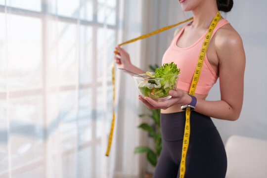 Woman holding salad and measuring tape representing healthy lifestyle