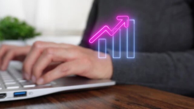 Economic progress. Close-up of a woman's hand working on a computer while pointing to a virtual bar graph icon with an upward-pointing arrow.