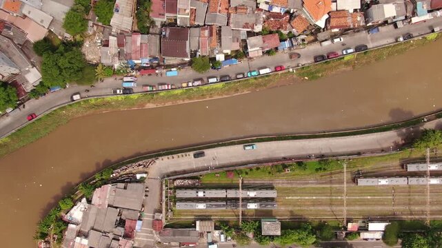 Top down aerial view of urban river canal, city highway, and railway system flowing through dense neighborhood. High angle shot of transportation infrastructure and water management in a megacity