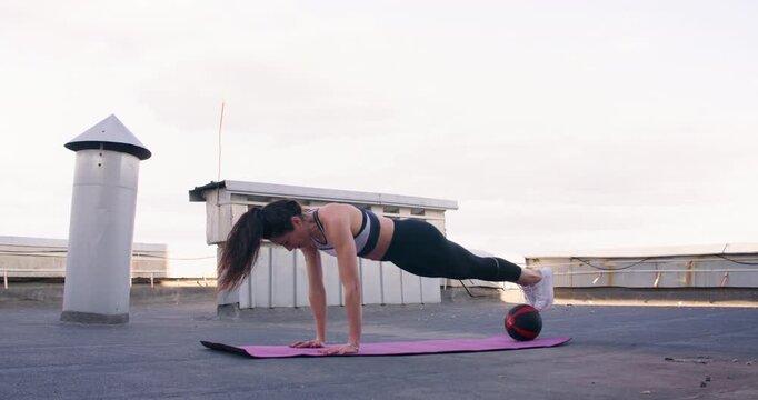 Plank ball training. Sport balance. Professional athlete woman enjoying fitness physical pilates exercise on yoga mat on rooftop outside.