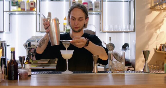 Cocktail recipe. Barkeeper strain. Worker pouring white liquid ingredient from metal shaker to glass. Professional pub technique tool.