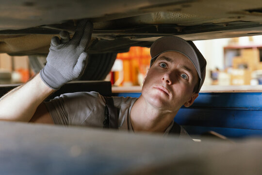 Technician examining the underside of a lifted vehicle during maintenance service at repair garage.