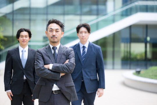 ビジネスチームを率いる40代のリーダーや管理職、社長や経営者、コンサルタントなどの3人複数のビジネスシーンカメラ目線笑顔　腕を組む転職や組織ビルディングや成功のイメージ