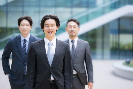 笑顔で歩くスーツで新卒採用や新人の若手ビジネスチームのポジティブ(前向き)なイメージ　転職や就活、採用などのカメラ目線の笑顔複数の横並び
