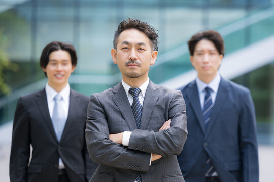 ビジネスチームを率いる40代のリーダーや管理職、社長や経営者、コンサルタントなどの3人複数のビジネスシーンカメラ目線笑顔　腕を組む転職や組織ビルディングや成功のイメージ