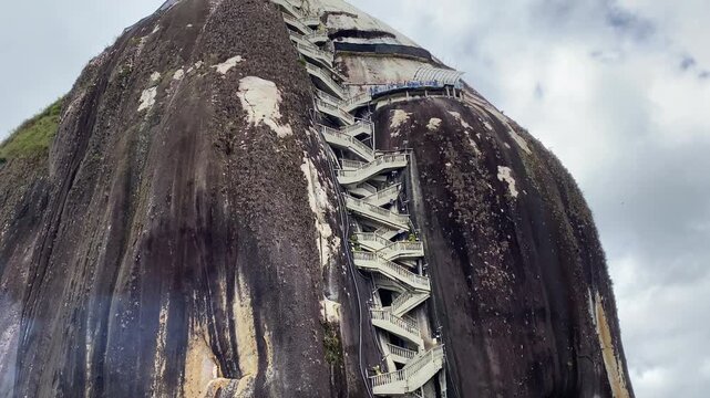 A medium drone pan following the iconic zig-zagging staircase of El Pe&ntilde;ol Rock (La Piedra). View of the stairs climbing the massive monolith in Guatap&eacute;, Antioquia, Colombia.