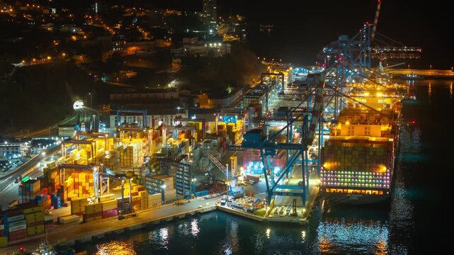 Aerial hyperlapse telephoto establishing of Valparaiso&rsquo;s main port, showing a giant cargo ship being unloaded and nighttime clearance procedures, Chile