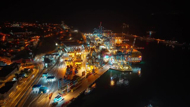 Aerial hyperlapse in orbit of the port of Valparaiso at night, displaying industrial unloading operations from a cargo ship and the import process, Chile