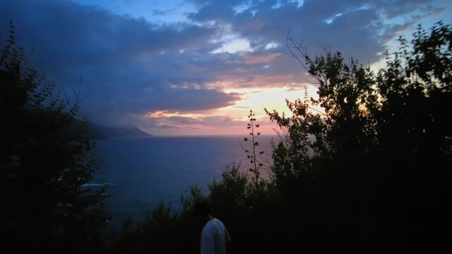 POV descending a dense mountain overlooking Choroni Bay with the sunset in the background, billowing clouds in the distance, Aragua, Venezuela