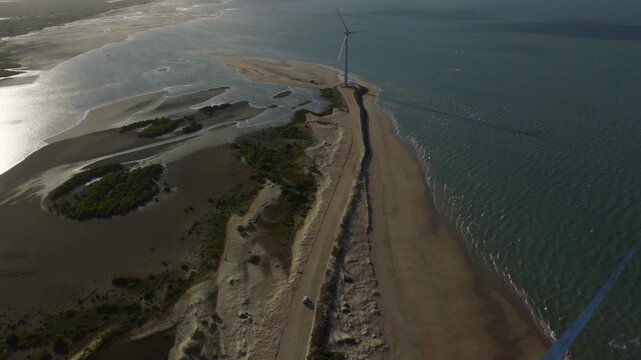 Coastal barrier spit near Ilha do Guajiru Itarema Cear&aacute; Brazil with wind turbines, sandy shoreline, tidal flats and access road separating lagoon and Atlantic Ocean, drone aerial shot