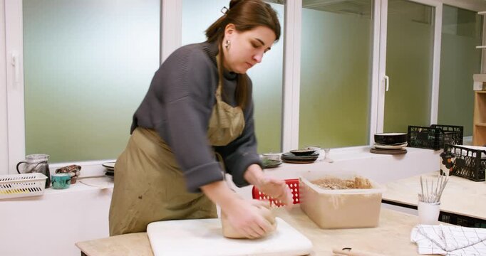 Potter occupation. Art therapy. Experienced woman master working with raw kneading clay in professional creative artisan workshop.