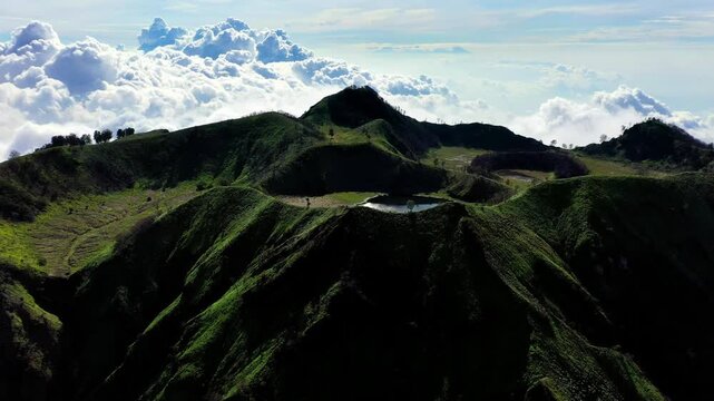 Aerial View Shot Extinct Volcanic Caldera Covered In Green Grass With Small Water Pond Inside Crater. Large Highlands of East Java Indonesia on Sunny Day Perfect For Travel 4k