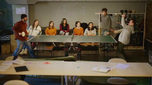 A group of happy students enjoys a lively game of table tennis in their common area. Friends and classmates gather to play and cheer, fostering teamwork and inclusion.