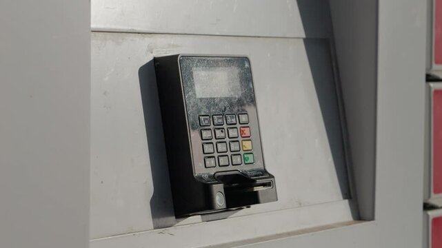 POS terminal is mounted on a wall outside. It faces the weather and is ready for wireless payments. The device is in use for quick transactions.