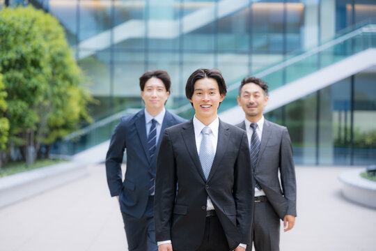 笑顔で歩くスーツで新卒採用や新人の若手ビジネスチームのポジティブ(前向き)なイメージ　転職や就活、採用などのカメラ目線の笑顔複数の横並び