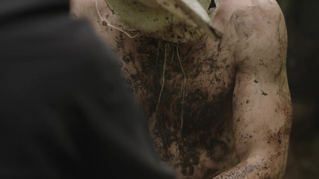 Man Helping Captive To Get Up With Head Covered With Sack And Body In Dirt. - closeup shot