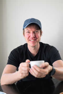 Smiling handsome Scandinavian Northern European man with blue eyes looking at camera in a cafe holding a coffee cup.