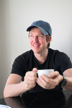 Smiling handsome Scandinavian Northern European man with blue eyes looking away thinking in a cafe holding a coffee cup.