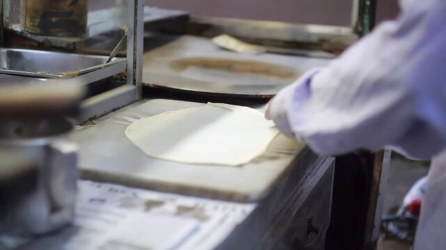 Close-up of a street food vendor skillfully stretching and flipping thin dough to make Martabak or Roti Canai on a marble counter. Authentic cooking.