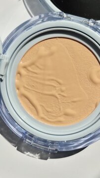 Vertical 4K macro of cosmetic cushion foundation. Close-up of beige liquid makeup texture in a compact case with light reflections.