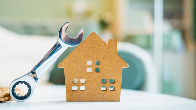 Home repair concept with wooden house model and wrench tool on white table. Maintenance, renovation, and construction service for real estate industry. High quality commercial photography.