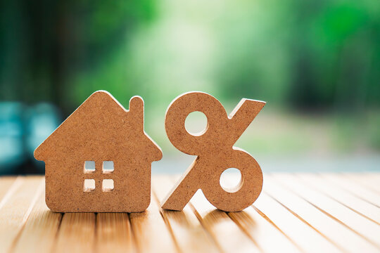 Real estate interest rate concept with wooden house model and percentage sign on wooden table. Mortgage, loan, property tax, and investment growth in housing market. Commercial stock image.