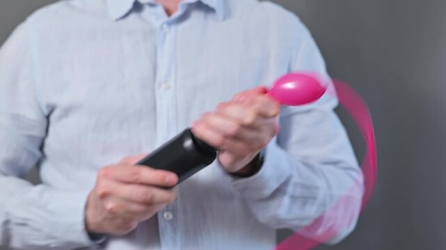 A person is using a pump to inflate a pink balloon in a basic indoor setting.