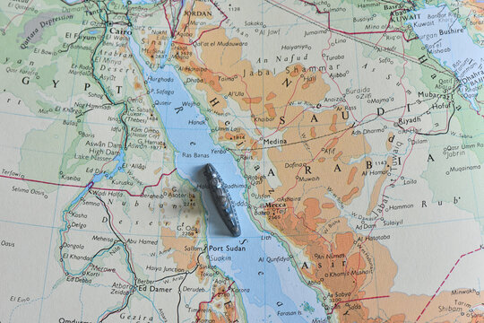 A small toy battleship placed on a vintage topographic map of the Red Sea, positioned between Egypt and Saudi Arabia, symbolizing maritime travel, shipping corridors, and naval strategy.