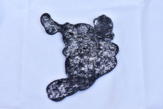 A top-down studio shot of a solid piece of recycled lead metal ingot obtained from smelting old waste batteries, isolated on a white background.