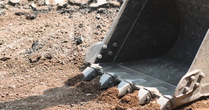 Excavator bucket leveling on gravel soil with visible steel teeth and track marks at an outdoor construction site
