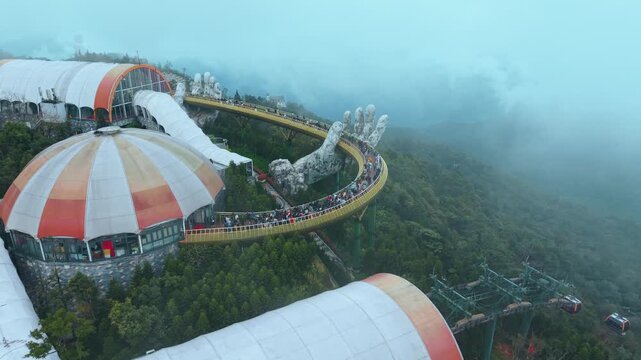 Golden Bridge architectural marvel in Ba Na Hills Vietnam supported by giant stone hands above forested mountains. Architecture concept combines creativity, engineering and scenic mountain tourism.