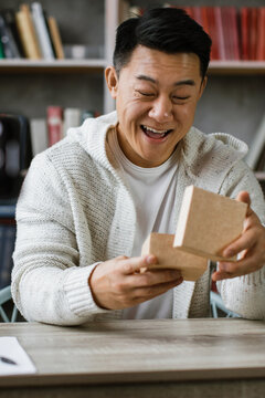A man with a joyful expression opens a small cardboard box while recording a video with his smartphone on a tripod